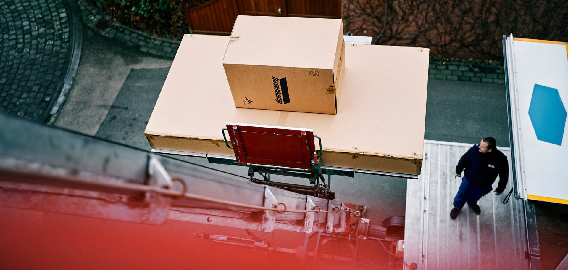 Ein Lastenaufzug zieht außen an einem Haus zwei Transportkisten mit hasenkamp-Aufdruck nach oben.