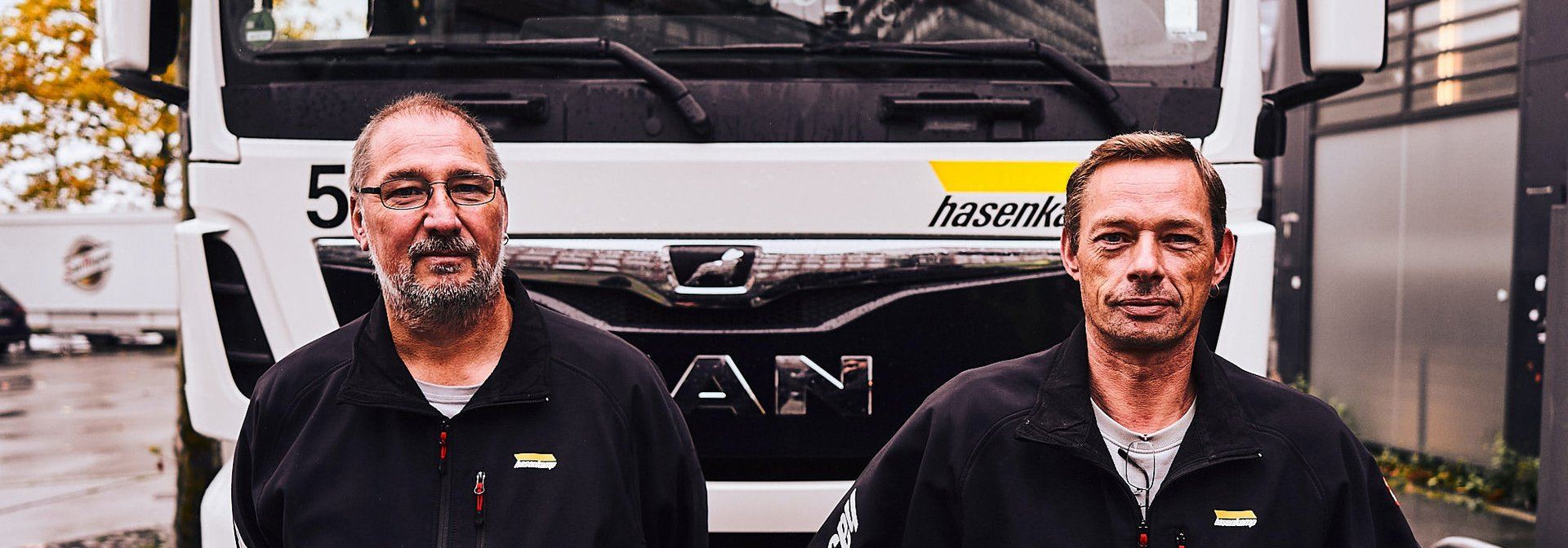 Zwei hasenkamp Mitarbeiter stehen vor ihrem LKW und lächeln in die Kamera.
